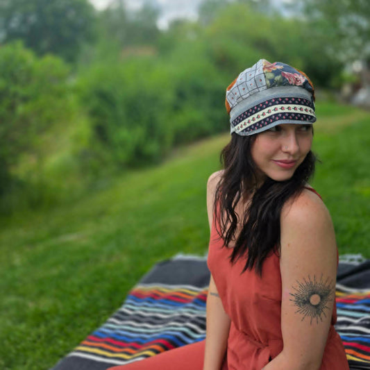 A woman wearing a colorful patterned knit cap sits outdoors on a striped blanket on a grassy hill, looking back over her shoulder.