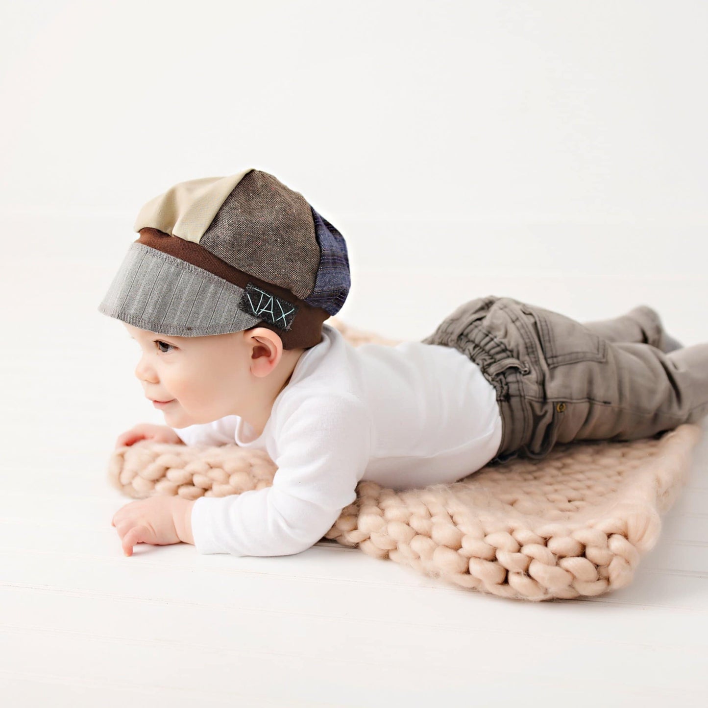 Baby lying on a rug wearing an Upcycled men's suit Newsboy hat with a decorative band