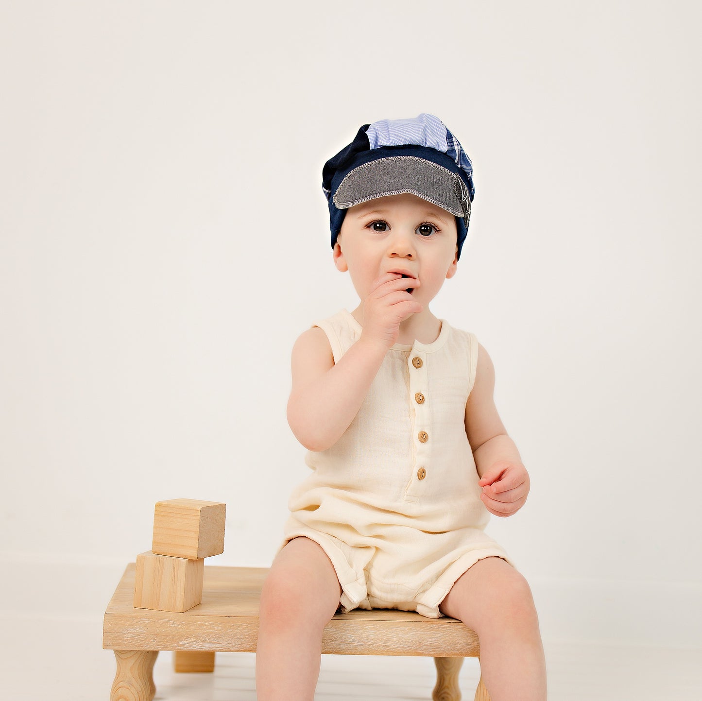 Toddler sitting on a wood stool with blocks wearing an Upcycled Blue Newsboy hat with decorative band