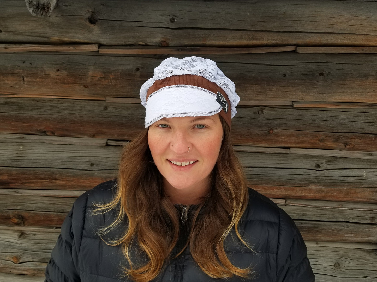 Lady with lace hat with decorative band against log cabin