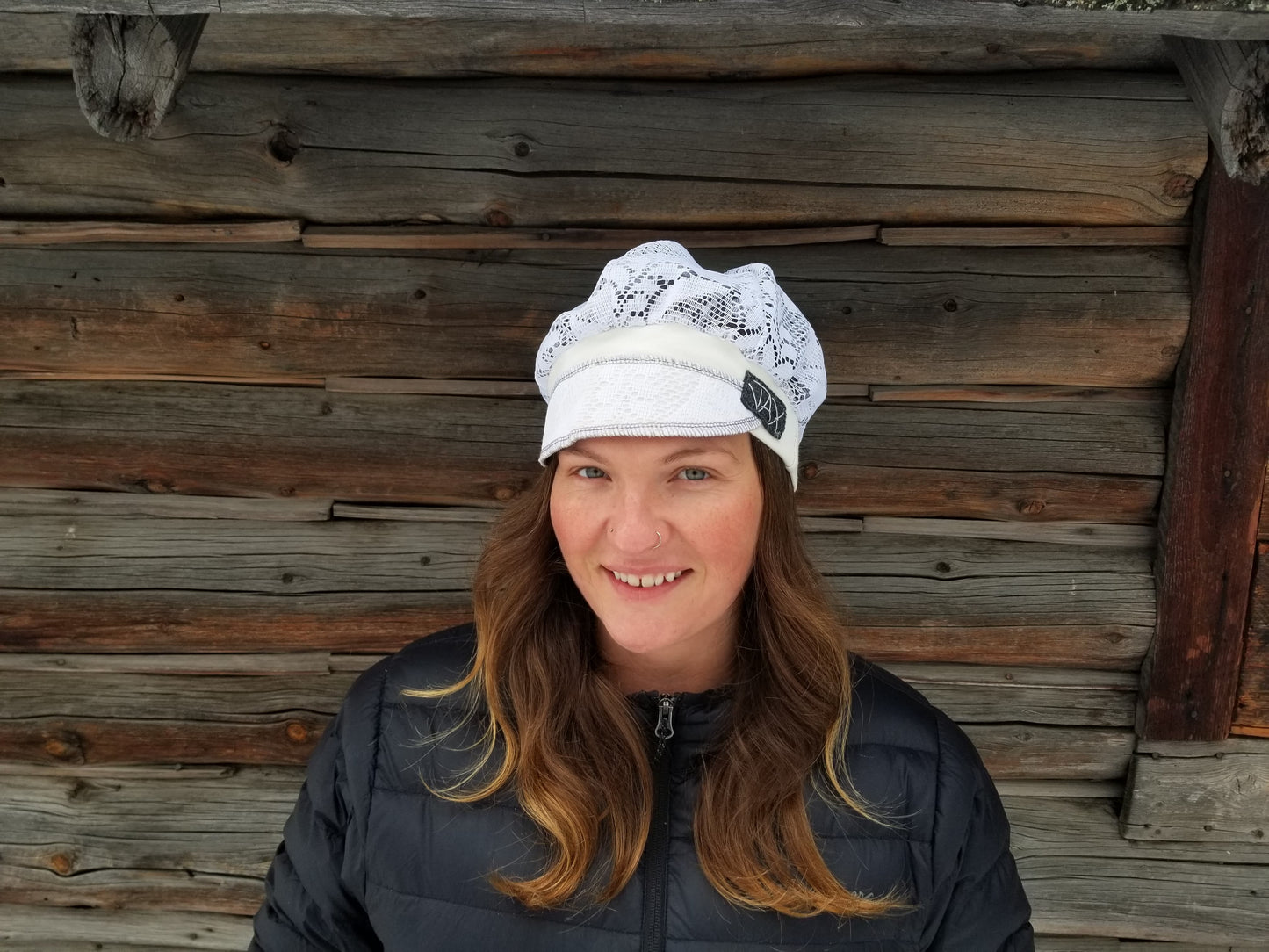 Lady with lace hat with decorative band against log cabin