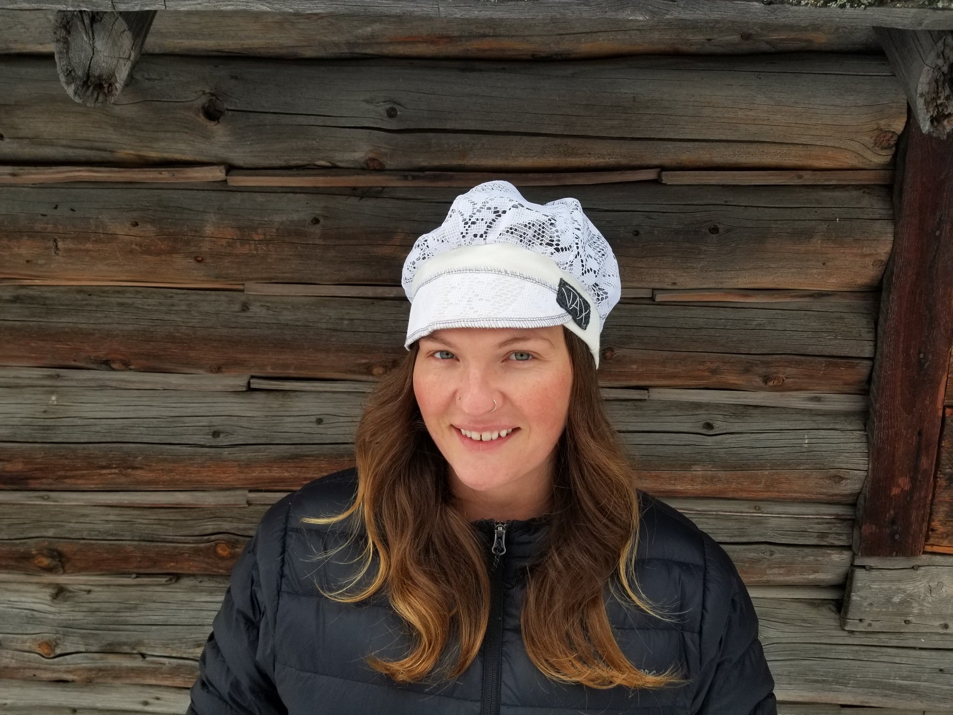 Lady with lace hat with decorative band against log cabin