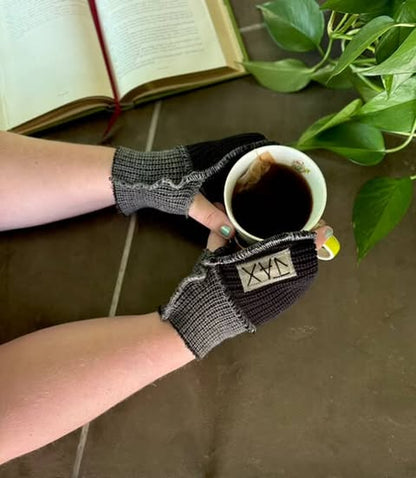 Person wearing textured gloves holding a cup of coffee with a book and plant in the background
