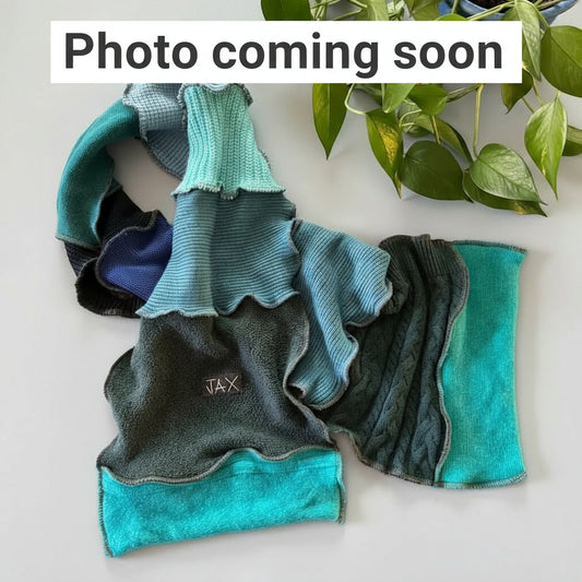 Teal tones scarf with 'JAX' branding on a white surface with green leaves in the background.