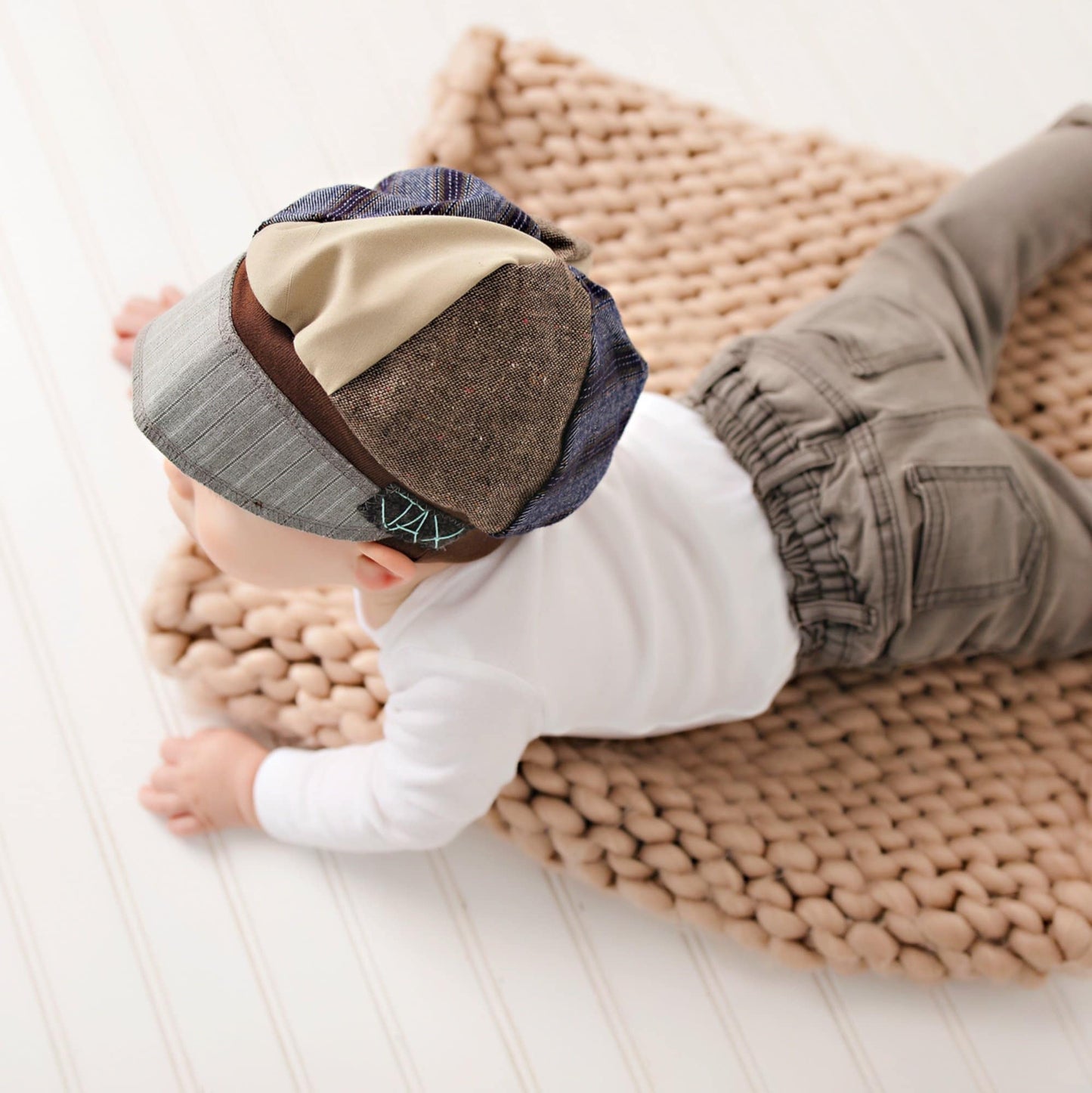 Baby wearing a brown upcycled from men's suits patchwork cap on a woven mat